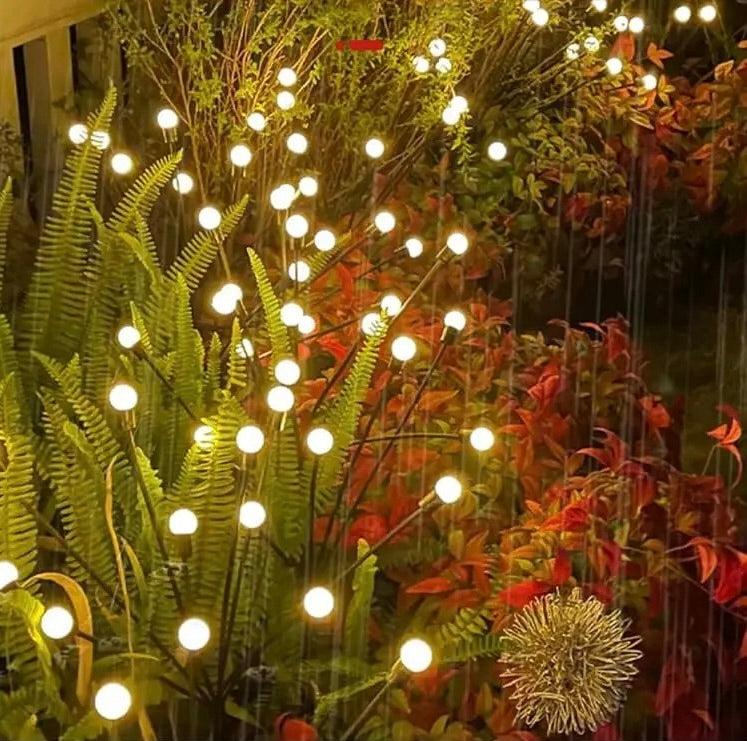 Lampes LED solaires lucioles installées dans un parterre de fougères et d’arbustes colorés