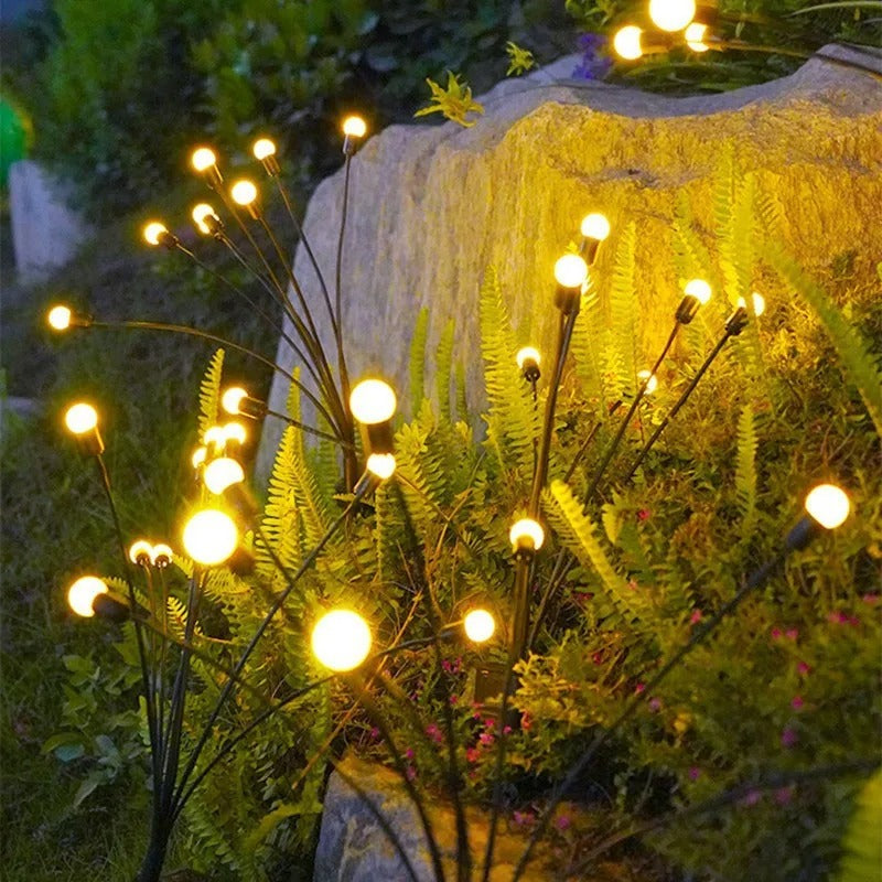 Guirlandes LED solaires effet lucioles plantées entre pierres et fougères au crépuscule